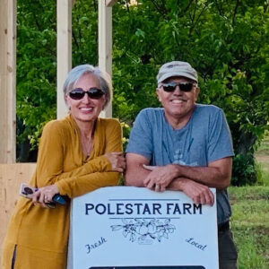 Smiling couple leaning on a Polestar Farm Fresh Local sign